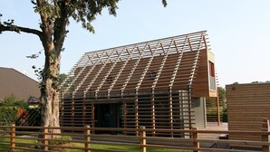 Un bâtiment moderne doté d’un toit à lattes et d’une clôture en bois au premier plan.