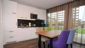 A modern kitchen with white cabinets, a wooden dining table, and purple chairs. - Chalet in Wendorf (Wendorf)