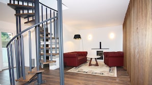 A modern living room with a spiral staircase, red sofas, a round coffee table, and a fireplace. - Chalet in Wendorf (Wendorf)