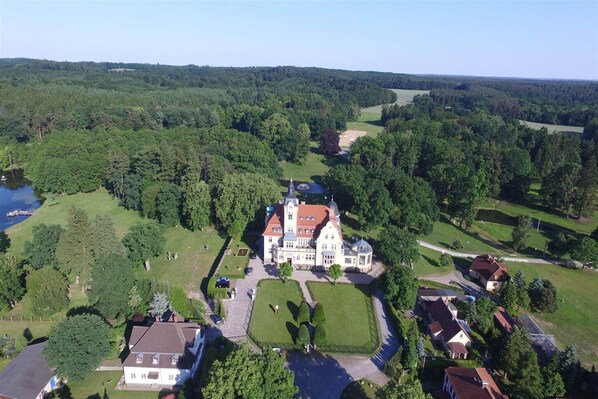 Vue aérienne d’un vaste domaine dont le bâtiment principal est entouré d’une végétation luxuriante et d’un lac.