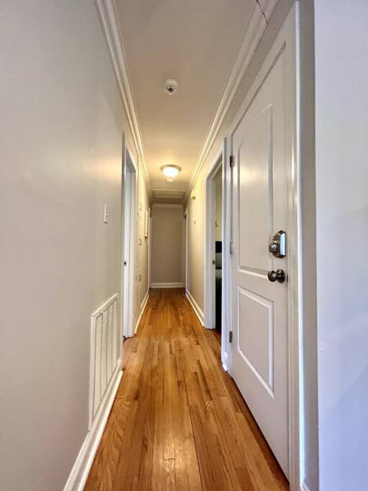 A narrow hallway with wooden flooring and white walls.