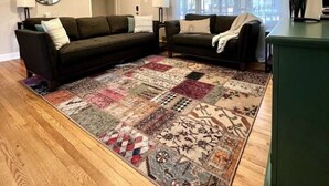 Un salon avec deux canapés sombres, un tapis à motifs, un plancher en bois, un ventilateur de plafond et un meuble vert.