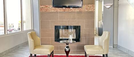 Una sala de estar moderna con chimenea, dos sillones, un tapete rojo y un televisor montado en la pared.