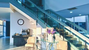 Un hall d’entrée moderne avec un escalier en verre, un comptoir d’accueil et un espace salon.