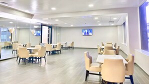 Une salle de conférence moderne, dotée de plusieurs tables et chaises, d’un grand téléviseur à écran plat fixé au mur et d’une grande fenêtre laissant entrer la lumière naturelle.