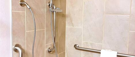Un espacio de ducha con ducha de mano, grifo empotrado y barra de apoyo.