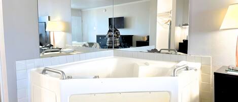 A modern bathroom with a corner bathtub, a large mirror, and a vanity with a lamp.