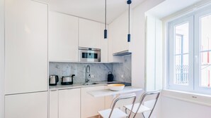 Une cuisine moderne avec des meubles blancs, un four en acier inoxydable, un plan de travail en marbre et une fenêtre donnant sur un immeuble.