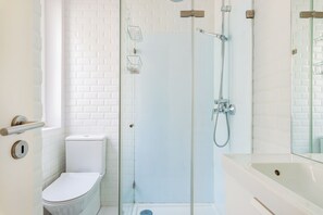 A modern bathroom with a glass-enclosed shower, a white toilet, and a large mirror above the sink.