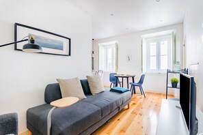 A modern living room with a grey sofa, a small round table, and a TV on a stand.