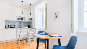 Une cuisine moderne avec des meubles blancs, un plancher en bois et un coin repas comprenant une table ronde et des chaises bleues.