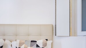 Un lit bien fait, avec un oreiller à motifs, une table de chevet et un luminaire fixé au mur.