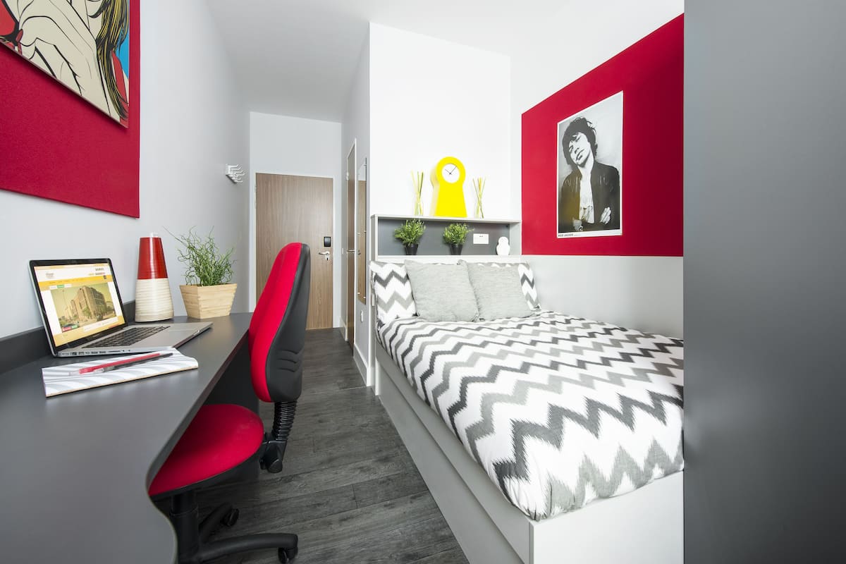 Quarto moderno com cama, escrivaninha, cadeira e uma parede de destaque vermelha.