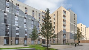 Un edificio de apartamentos moderno con varios balcones, un patio con árboles y fachada de ladrillo.