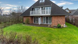 A two-story house with a balcony, brick exterior, and a well-maintained lawn. - Ferienwohnung in St. Peter-Ording (St. Peter-Ording)
