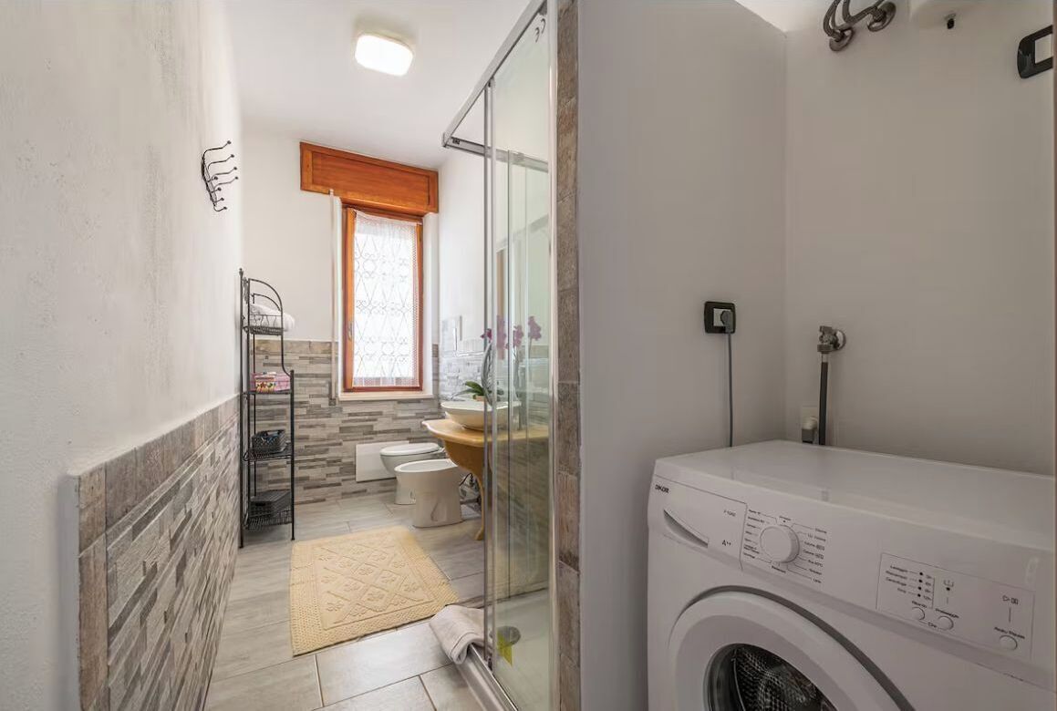Un bagno moderno con box doccia in vetro, lavabo a incasso e lavatrice a carica frontale.