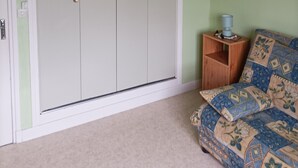 Una habitación con un armario grande, una mesita de noche de madera pequeña con una lámpara, y un edredón estampado.