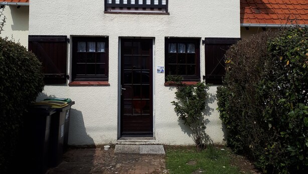 Una casa de dos pisos con fachada blanca, una puerta principal negra y una ventana pequeña con persiana blanca.