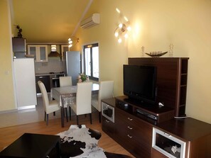 Un salon moderne doté d’un téléviseur à écran plat, d’un meuble de rangement en bois et d’un coin repas avec une table et des chaises.