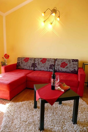 Een gezellige woonkamer met een rode bank, een kleine tafel met een fles en glas, en een decoratieve lamp.