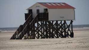 Una estructura de madera para muelle con un edificio que dice 'Toiletten' en la parte superior, ubicada en una playa arenosa.