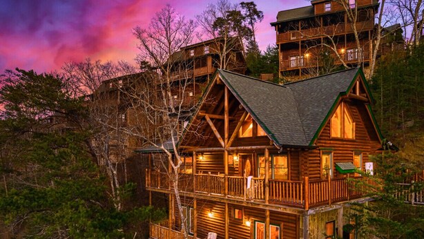 A multi-story log cabin with balconies, surrounded by trees. - NERF War-Family Lodge-Theater-HotTub-GlowParty (Sevierville)