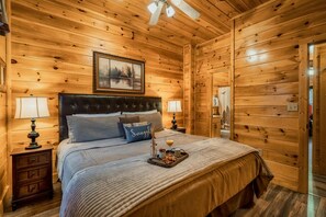 A wooden-paneled bedroom with a bed, two bedside lamps, a framed picture above the bed, and a tray with snacks on the bed. - NERF War-Family Lodge-Theater-HotTub-GlowParty (Sevierville)