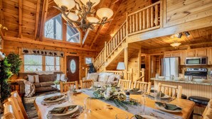A wooden cabin interior with a dining area, kitchen, and a staircase. - NERF War-Family Lodge-Theater-HotTub-GlowParty (Sevierville)