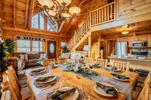 A wooden cabin interior with a dining area, kitchen, and a staircase.