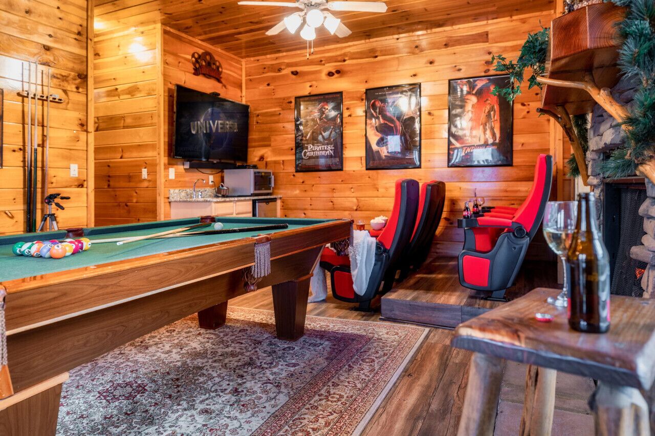 Un intérieur en bois avec une table de billard, des chaises rouges, un téléviseur et des affiches encadrées.