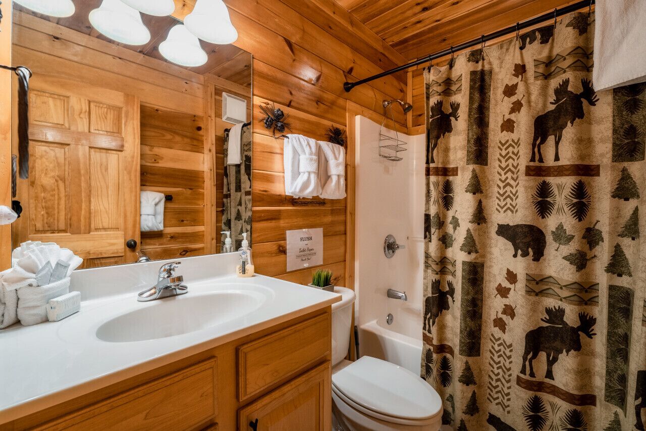 A wooden cabin bathroom with a sink, toilet, and shower curtain featuring animal prints.
