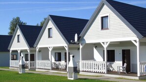 A row of white cabins with dark roofs, each featuring a porch with chairs and a grill. - Holiday homes with terraces, close to the beach (Ustronie Morskie)