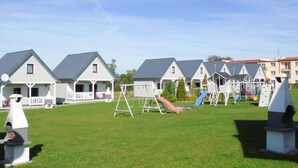 A row of white houses with grey roofs, a playground with swings and slides, and a clear blue sky. - Holiday homes with terraces, close to the beach (Ustronie Morskie)