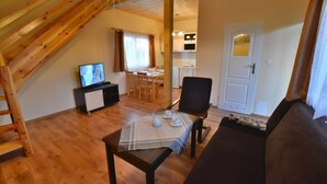 A cozy living room with a wooden ceiling, a dining area with a table set for two, and a kitchenette in the background. - Holiday homes with terraces, close to the beach (Ustronie Morskie)