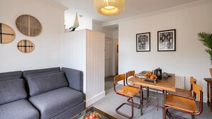 Ein modernes Wohnzimmer mit grauem Sofa, einem Holzesstisch mit Stühlen und einem Couchtisch mit Obst.