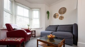 Ein Wohnzimmer mit einem roten Sessel, einem grauen Sofa und einem Glastisch mit Obst.