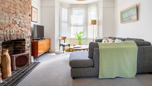 Een woonkamer met een bakstenen muur, een open haard, een bank, een televisie en een plant.