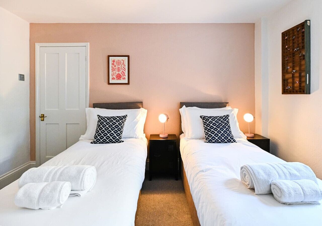 A double room with two beds, each with white linens and black patterned pillows. There are two bedside tables with lamps, and towels are neatly folded on the beds.