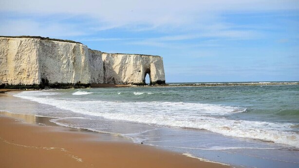 Una playa con acantilados blancos y un arco natural en el mar.