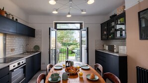Una cocina moderna con una mesa de comedor de madera, armarios negros y vistas al jardín a través de una puerta abierta.