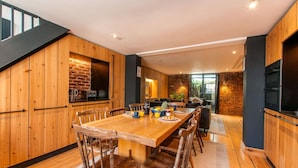 Une cuisine moderne avec des meubles en bois, une grande table à manger et une cheminée en briques intégrée.