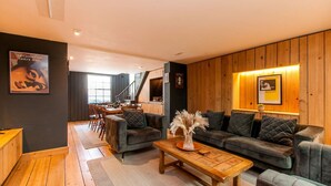 Un salon moderne avec des canapés sombres, une table basse en bois et un coin repas comprenant des chaises et une table.