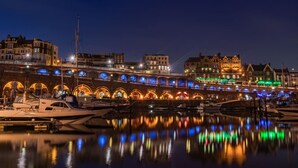 Un pont au bord de l’eau, avec des arches illuminées qui se reflètent dans l’eau.
