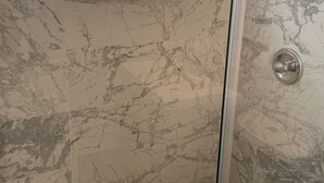 A bathroom with marble tiles, a glass shower enclosure, and a window.