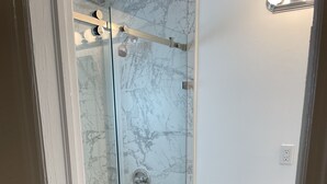A bathroom with a glass-enclosed shower, a white toilet, and a marble-tiled wall.