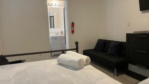 A bedroom with a bed, a black sofa, a dresser, and a mirror.