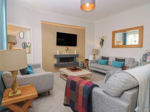 A modern living room with a fireplace, grey sofas, a coffee table, and a flat-screen TV mounted on the wall.
