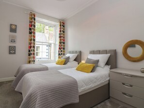 A bedroom with two beds, a bedside table, a nightstand, and a window with curtains.
