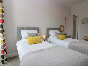 Ein Hotelzimmer mit zwei Betten, einem Nachttisch mit Lampe, einem runden Spiegel und einer Tür mit Handtuchhalter.