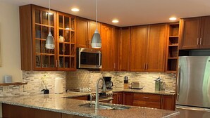 Eine moderne Küche mit Holzschränken, einem Edelstahlkühlschrank, einer Granitarbeitsplatte und drei Barhocker.